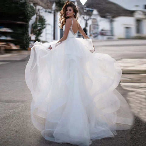 Vestido de novia de corte princesa con tirantes finos, espalda descubierta y delicados volantes con cuentas. 