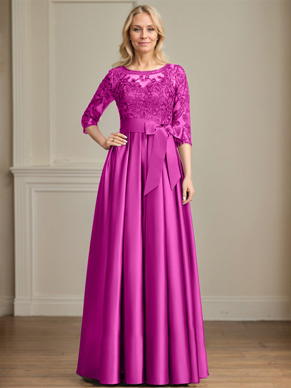 Robe de mariée longue en satin et dentelle, coupe trapèze, décolleté illusion, ornée d'un nœud à sequins. 