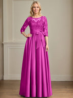 Robe de mariée longue en satin et dentelle, coupe trapèze, décolleté illusion, ornée d'un nœud à sequins. 