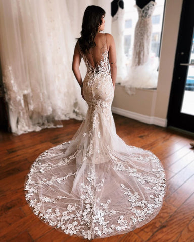 Robe de mariée sirène longue et glamour, sans manches, dos nu et décolleté en V, ornée de dentelle.