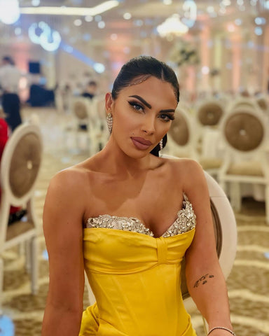 Precioso vestido largo de fiesta amarillo sin tirantes estilo sirena con joyas y abertura.