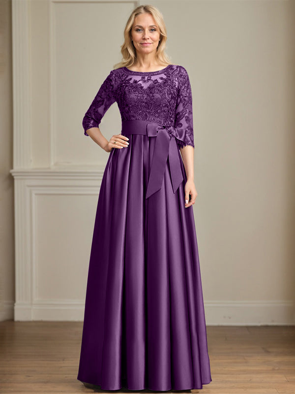 Robe de mariée longue en satin et dentelle, coupe trapèze, décolleté illusion, ornée d'un nœud à sequins. 