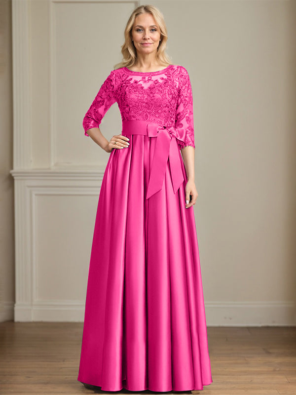 Robe de mariée longue en satin et dentelle, coupe trapèze, décolleté illusion, ornée d'un nœud à sequins. 
