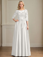 Robe de mariée longue en satin et dentelle, coupe trapèze, décolleté illusion, ornée d'un nœud à sequins. 