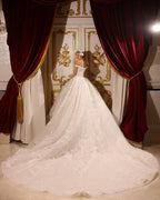 Vestido de novia largo de corte A, con hombros descubiertos, apliques, pedrería y cola.