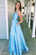 Robe de bal bleue longue en satin avec poches, bretelles spaghetti et coupe trapèze.