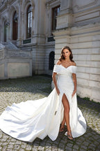 Vestido de novia de corte sirena, estilo princesa, con hombros descubiertos, abertura frontal y volantes.