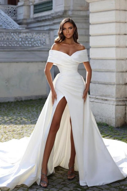 Vestido de novia de corte sirena, estilo princesa, con hombros descubiertos, abertura frontal y volantes.