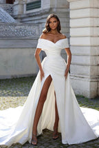 Vestido de novia de corte sirena, estilo princesa, con hombros descubiertos, abertura frontal y volantes.