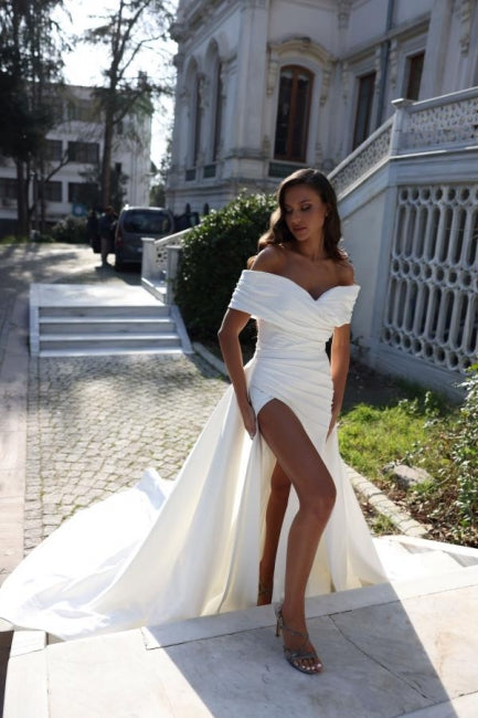 Vestido de novia de corte sirena, estilo princesa, con hombros descubiertos, abertura frontal y volantes.