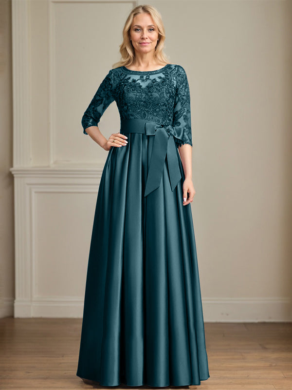 Robe de mariée longue en satin et dentelle, coupe trapèze, décolleté illusion, ornée d'un nœud à sequins. 
