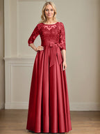 Robe de mariée longue en satin et dentelle, coupe trapèze, décolleté illusion, ornée d'un nœud à sequins. 