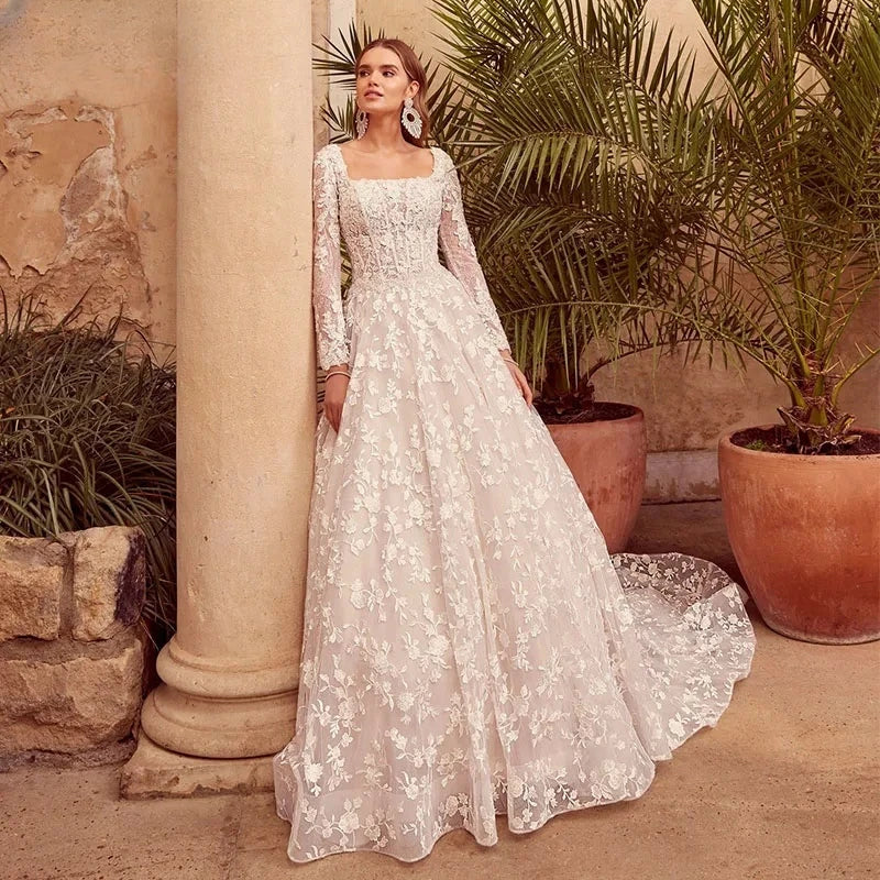 Vestido de novia corte A con escote cuadrado, apliques de encaje, mangas largas y cola de corte.