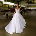 Robe de mariée blanche en organza et tulle, coupe trapèze, ornée de cristaux et à manches longues, avec col transparent. 