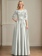 Robe de mariée longue en satin et dentelle, coupe trapèze, décolleté illusion, ornée d'un nœud à sequins. 