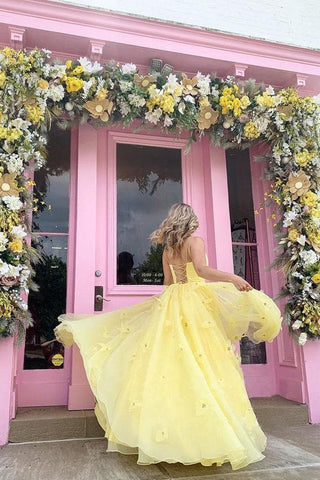 Vestido de fiesta amarillo con tirantes, corpiño de tul, flores 3D y espalda con cordones.