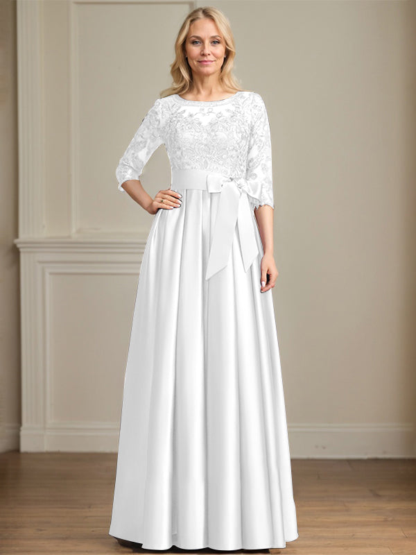 Robe de mariée longue en satin et dentelle, coupe trapèze, décolleté illusion, ornée d'un nœud à sequins. 