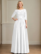 Robe de mariée longue en satin et dentelle, coupe trapèze, décolleté illusion, ornée d'un nœud à sequins. 