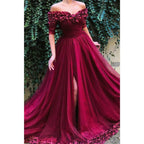 Vestido largo de noche formal, corte en A, de tul burdeos, con hombros descubiertos, apliques y abertura. 