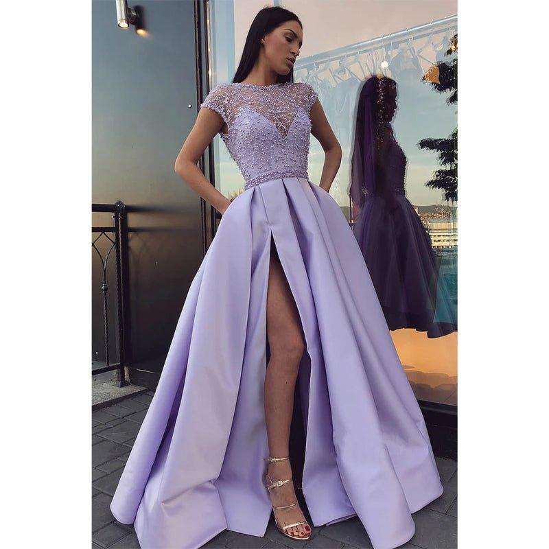 Vestido largo de fiesta de corte A, color lila, con escote ilusión de satén, encaje, pedrería, abertura alta y bolsillos. 