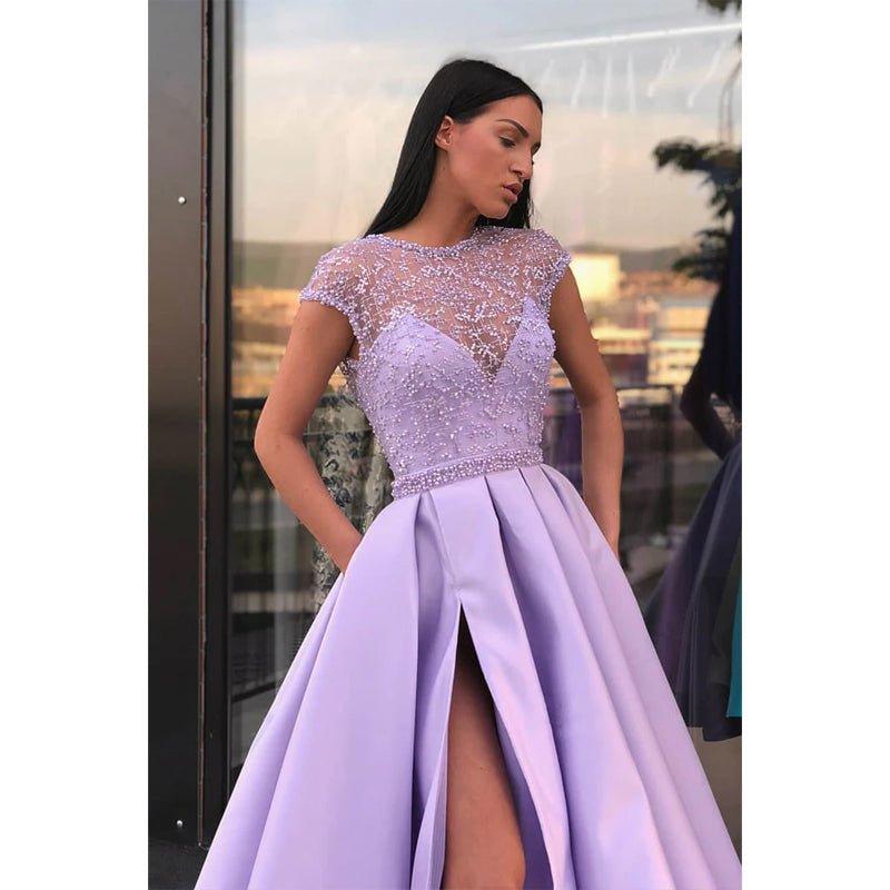 Vestido largo de fiesta de corte A, color lila, con escote ilusión de satén, encaje, pedrería, abertura alta y bolsillos. 