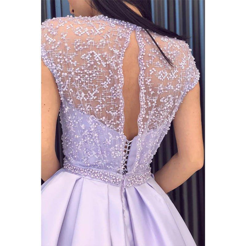 Vestido largo de fiesta de corte A, color lila, con escote ilusión de satén, encaje, pedrería, abertura alta y bolsillos. 