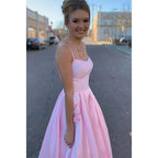 Vestido largo de fiesta rosa satinado de corte evasé con tirantes finos, escote redondo y bolsillos. 