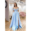 Vestido largo de fiesta de corte A, color azul celeste satinado, con hombros descubiertos, abertura alta y bolsillos. 