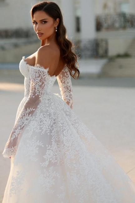Robe de mariée blanche longue en dentelle, coupe trapèze, épaules dénudées et manches longues, ravissante.