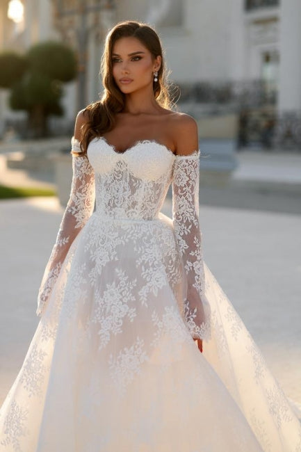 Robe de mariée blanche longue en dentelle, coupe trapèze, épaules dénudées et manches longues, ravissante.