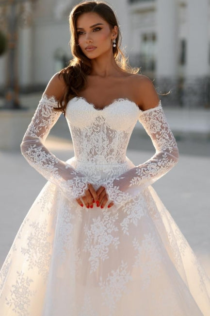 Robe de mariée blanche longue en dentelle, coupe trapèze, épaules dénudées et manches longues, ravissante.