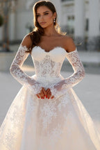 Robe de mariée blanche longue en dentelle, coupe trapèze, épaules dénudées et manches longues, ravissante.