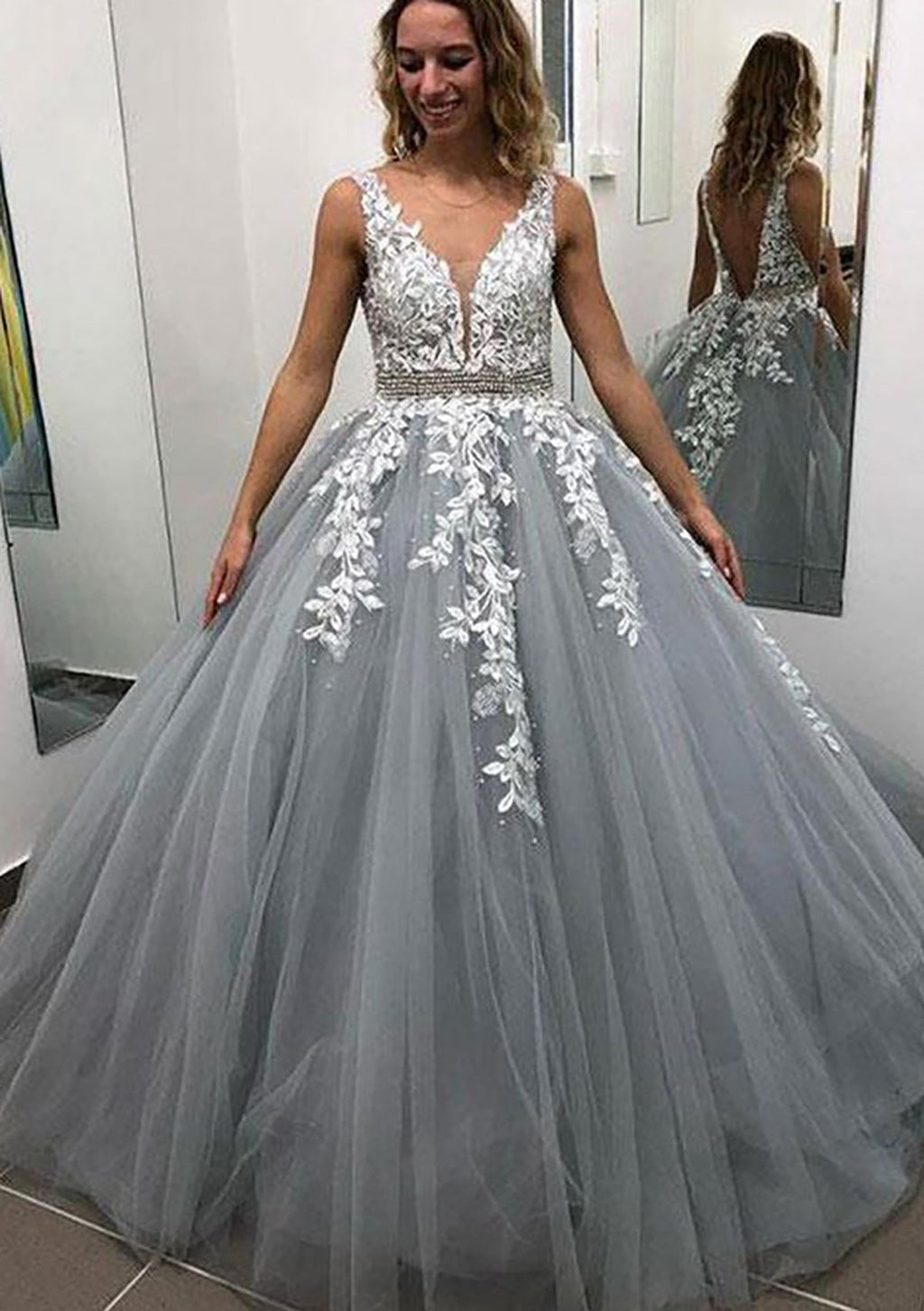 Robe de bal longue sans manches en tulle, arrivant au sol, ornée de dentelle et de perles appliquées.