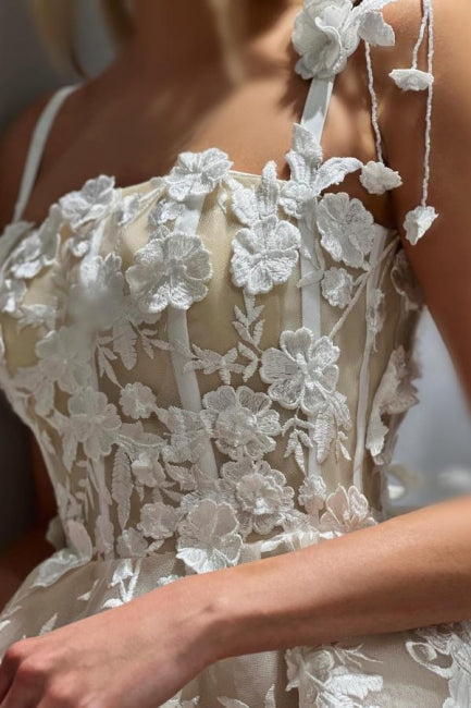 Magnifique robe de mariée courte ivoire sans manches, coupe trapèze, en tulle et dentelle, à fines bretelles spaghetti et ornée d'appliqués.