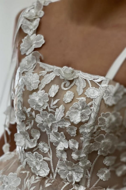 Magnifique robe de mariée courte ivoire sans manches, coupe trapèze, en tulle et dentelle, à fines bretelles spaghetti et ornée d'appliqués.