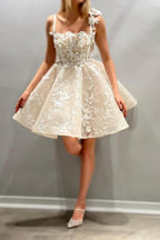 Magnifique robe de mariée courte ivoire sans manches, coupe trapèze, en tulle et dentelle, à fines bretelles spaghetti et ornée d'appliqués.