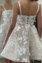Magnifique robe de mariée courte ivoire sans manches, coupe trapèze, en tulle et dentelle, à fines bretelles spaghetti et ornée d'appliqués.