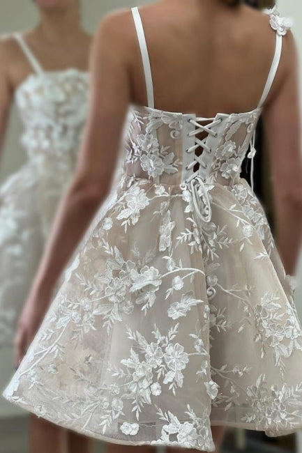 Magnifique robe de mariée courte ivoire sans manches, coupe trapèze, en tulle et dentelle, à fines bretelles spaghetti et ornée d'appliqués.