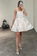 Magnifique robe de mariée courte ivoire sans manches, coupe trapèze, en tulle et dentelle, à fines bretelles spaghetti et ornée d'appliqués.