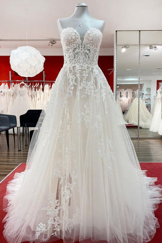 Magnifique robe de mariée longue en tulle ivoire, sans bretelles, de coupe trapèze, ornée d'appliqués de dentelle.