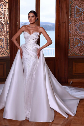 Magnifique robe de mariée blanche sans manches à décolleté cœur ornée de perles et traîne amovible.