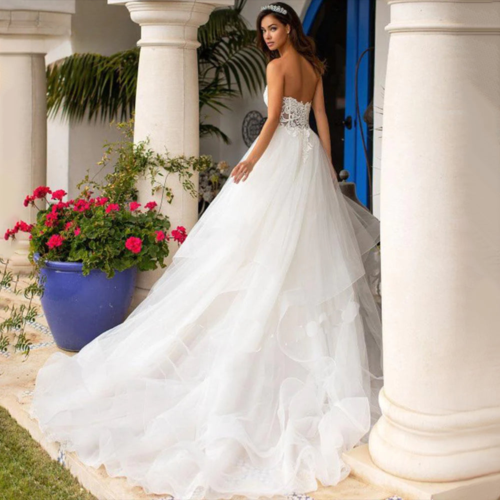 Vestido de novia de lujo estilo princesa, con espalda descubierta, corpiño de lentejuelas y pedrería, escote corazón, apliques de encaje y falda de organza con volumen. 