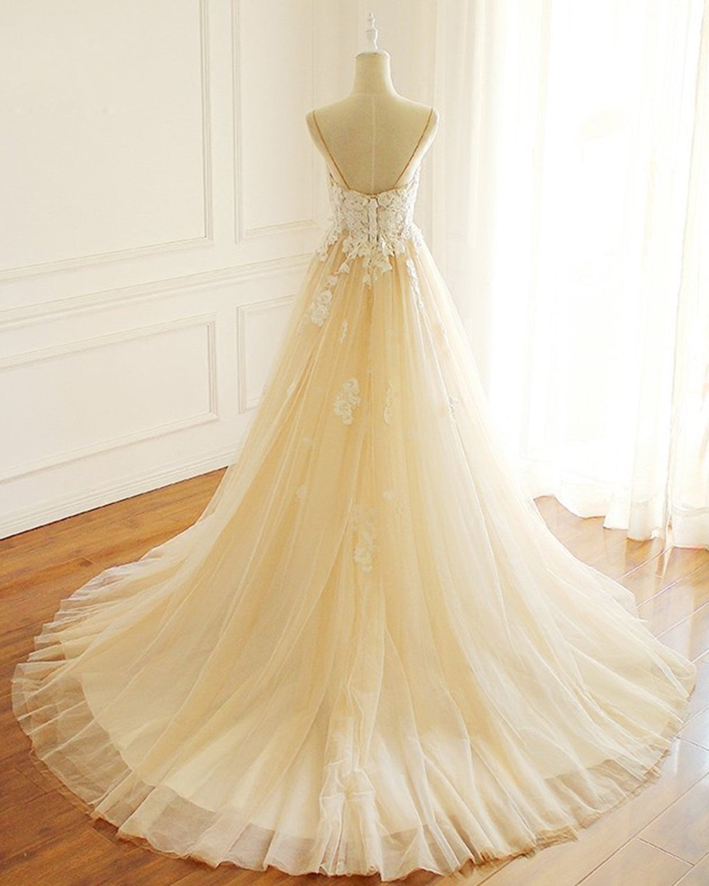 Robe de mariée longue en tulle champagne, coupe trapèze, décolleté cœur et traîne spaghetti, ornée de spaghettis.