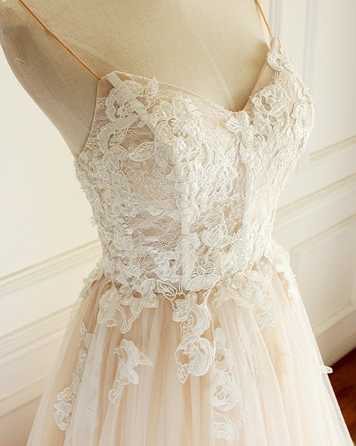 Robe de mariée longue en tulle champagne, coupe trapèze, décolleté cœur et traîne spaghetti, ornée de spaghettis.