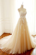 Robe de mariée longue en tulle champagne, coupe trapèze, décolleté cœur et traîne spaghetti, ornée de spaghettis.