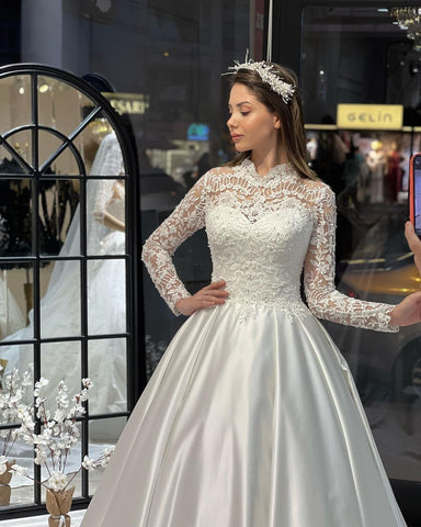 Robe de mariée trapèze en satin, charmante, longue jusqu'au sol, manches longues, col rond, ornée de volants.