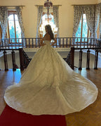 Robe de mariée charmante en dentelle, longue jusqu'au sol, décolleté cœur, manches longues et coupe trapèze, ornée de fleurs.