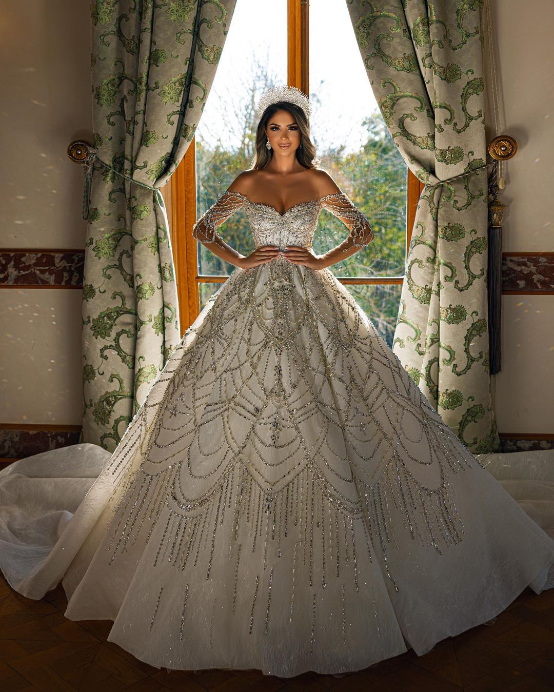 Robe de mariée charmante en dentelle, longue jusqu'au sol, décolleté cœur, manches longues et coupe trapèze, ornée de fleurs.