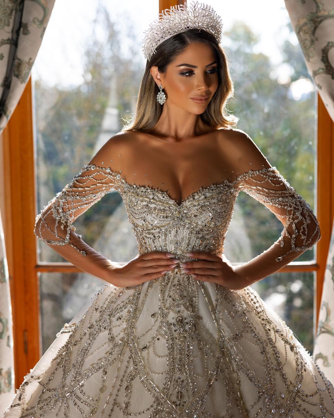 Robe de mariée charmante en dentelle, longue jusqu'au sol, décolleté cœur, manches longues et coupe trapèze, ornée de fleurs.