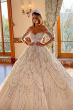 Robe de mariée charmante en dentelle, longue jusqu'au sol, décolleté cœur, manches longues et coupe trapèze, ornée de fleurs.